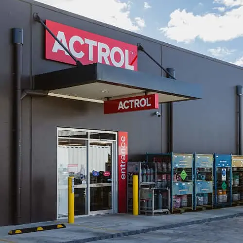 Actrol store entrance with red signage above glass doors, yellow bollards, and product displays visible outside.