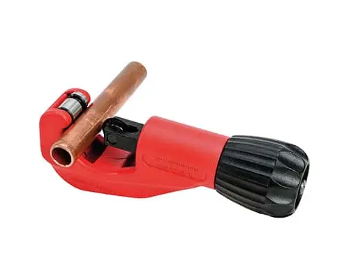 Red and black pipe cutter with copper pipe inserted, showing cutting wheel and adjustment knob on white background.