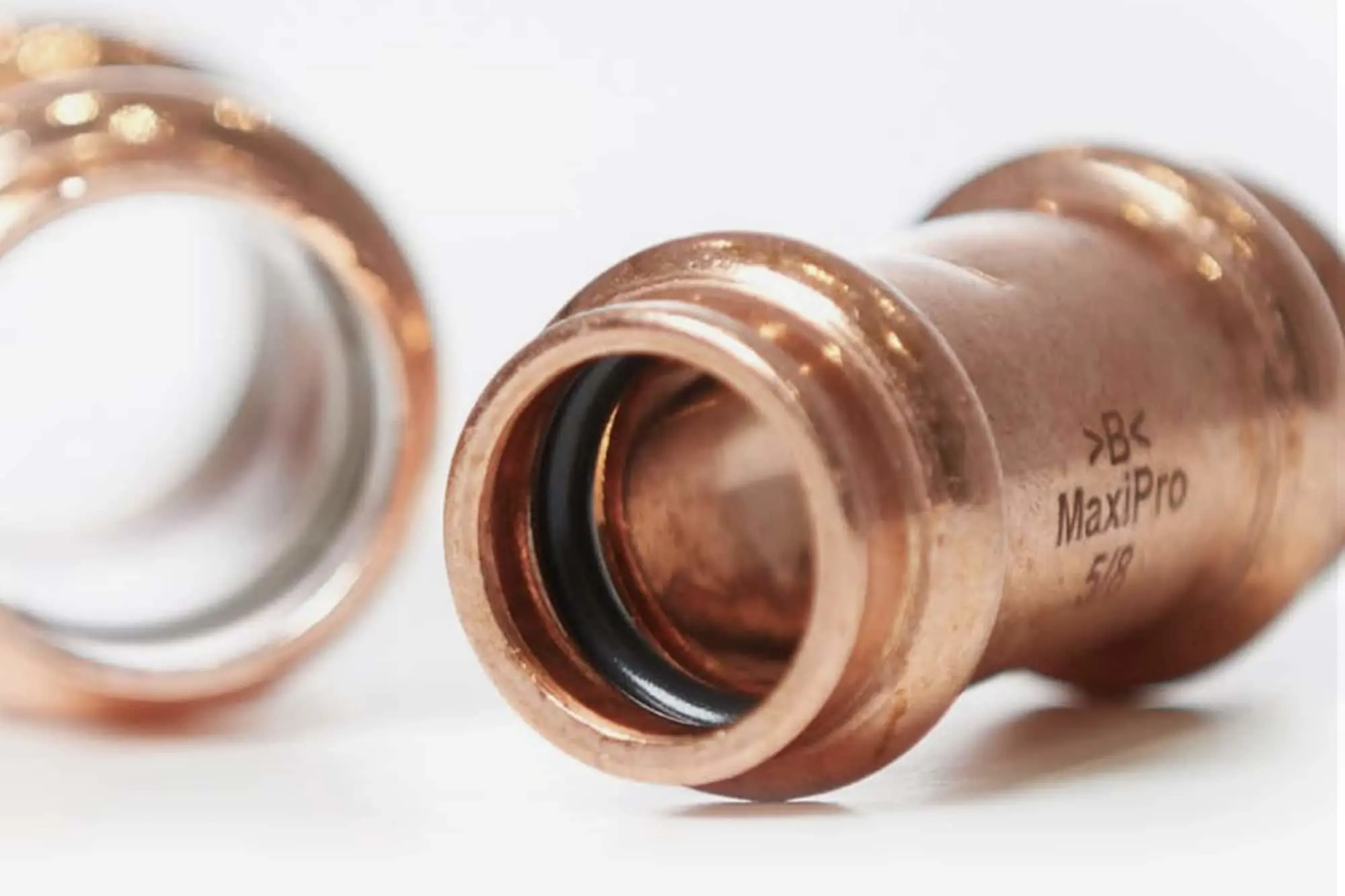 Copper pipe fittings with black rubber seals on a white surface, with MaxiPro branding visible on the metal.
