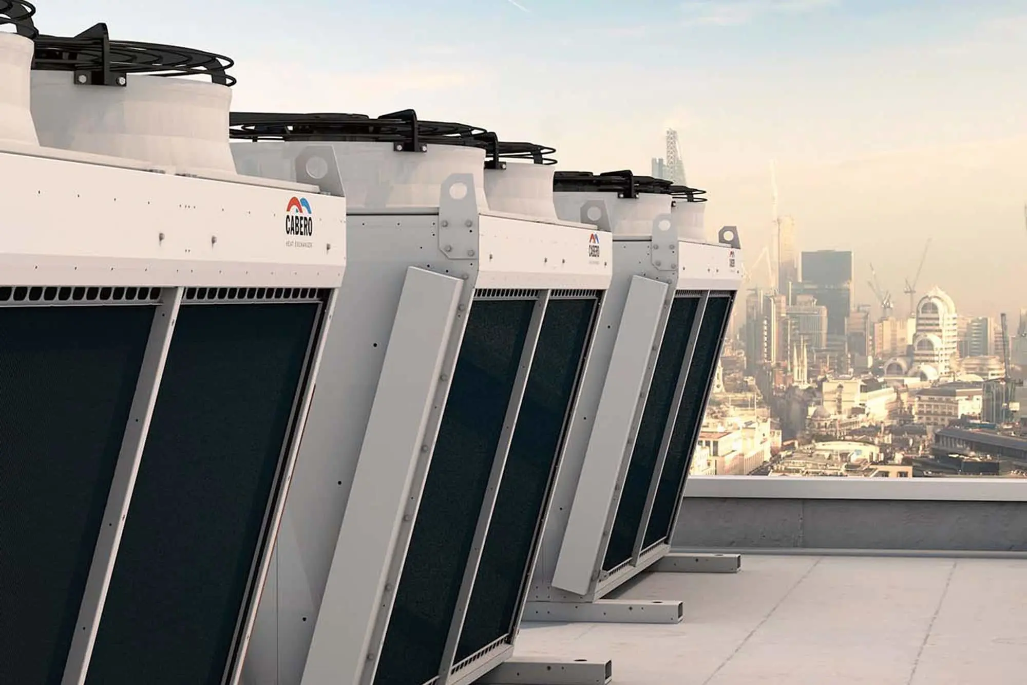 Row of white industrial cooling units with black fans on a rooftop with city skyline in background