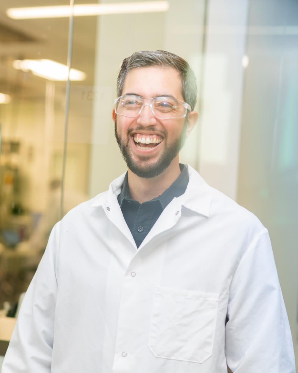 Man in lab coat and safety glasses laughing