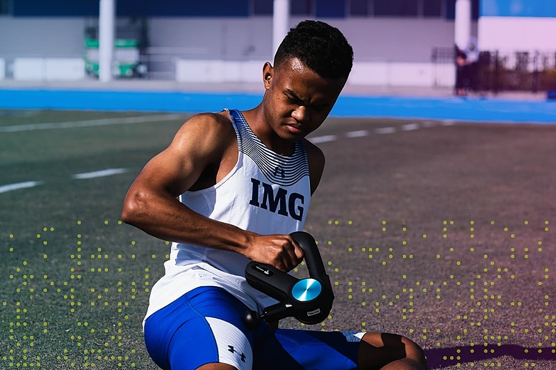IMG Academy athlete seated on the track using a recovery device, representing mental strength and resilience while overcoming injury.