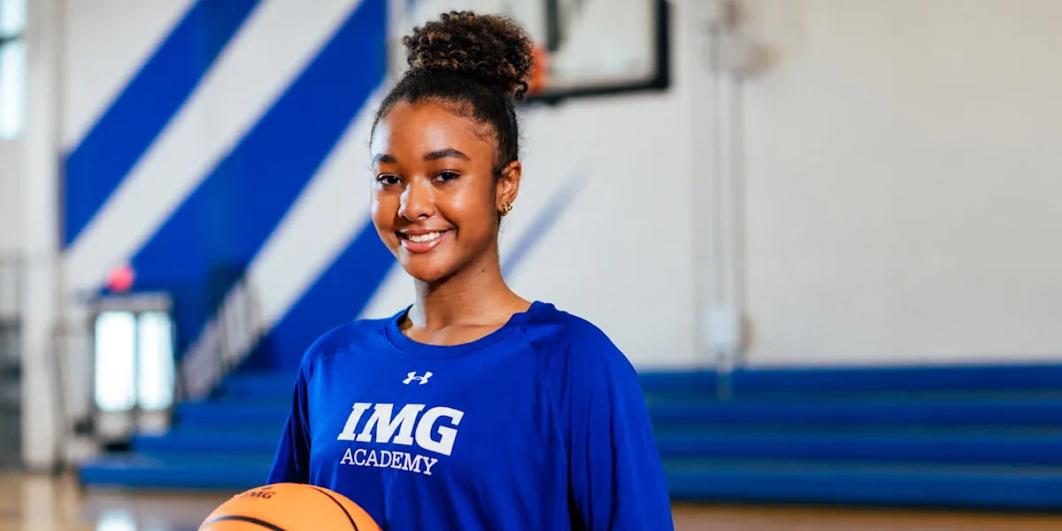 A smiling basketball player holds a ball in a gym.
