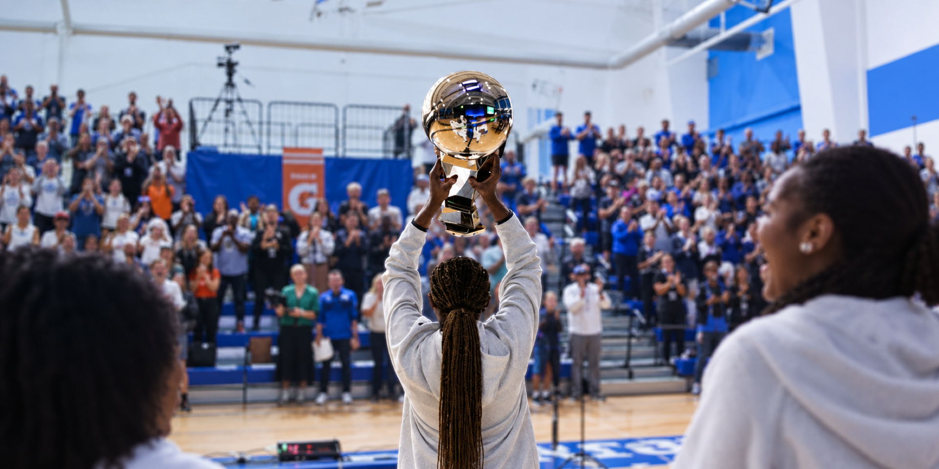 A student holds a trophy overhead in a crowded gymnasium.