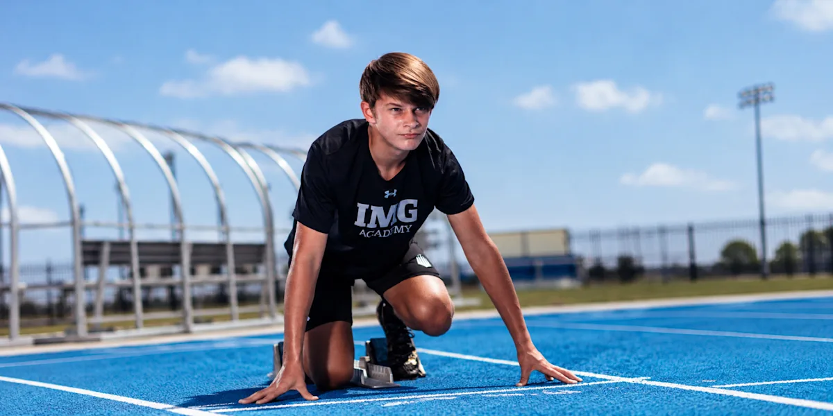 A sprinter crouches at starting blocks on a blue track.
