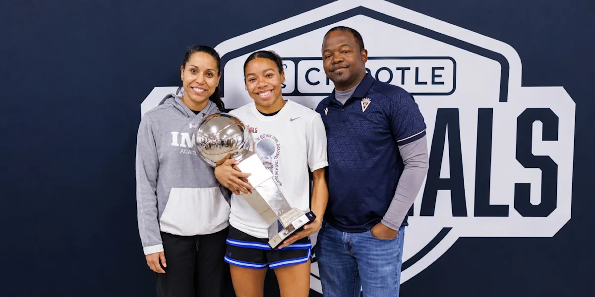A student-athlete holds a trophy while posing with two adults.