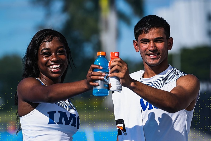 IMG Academy student-athletes smiling and clinking sports drink bottles on an outdoor field, celebrating hydration, teamwork, and recovery after training.