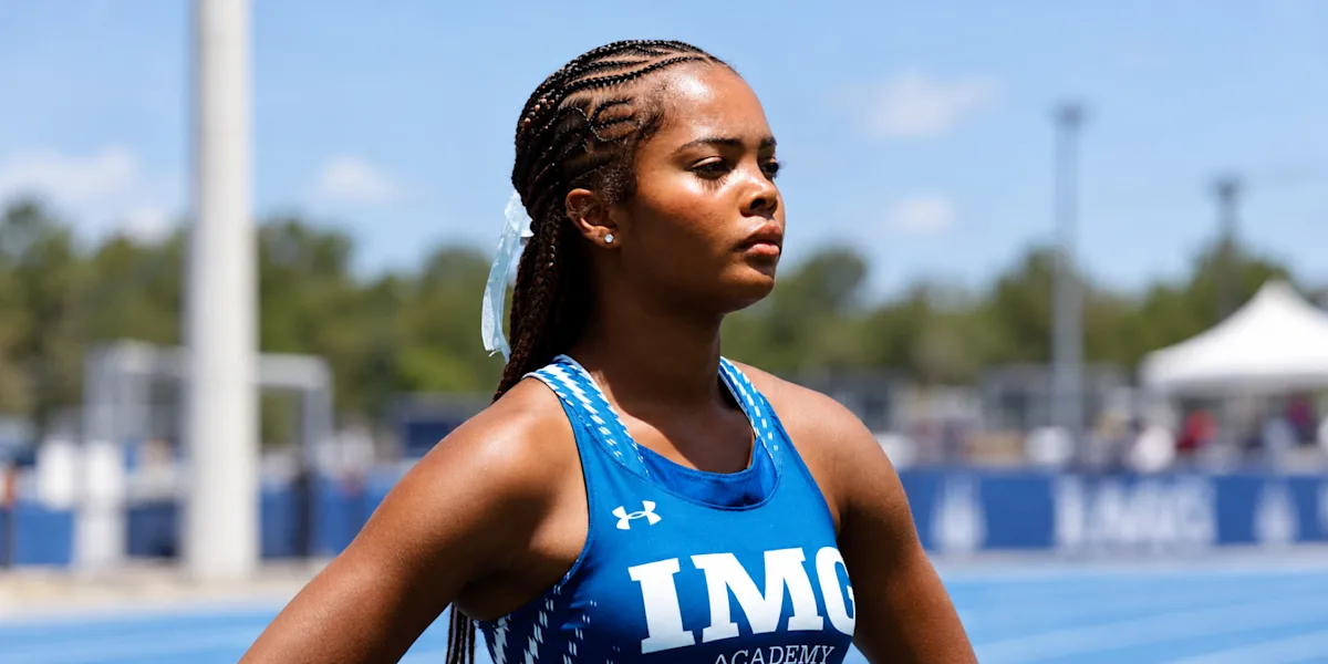 A track athlete stands focused beside an outdoor track.