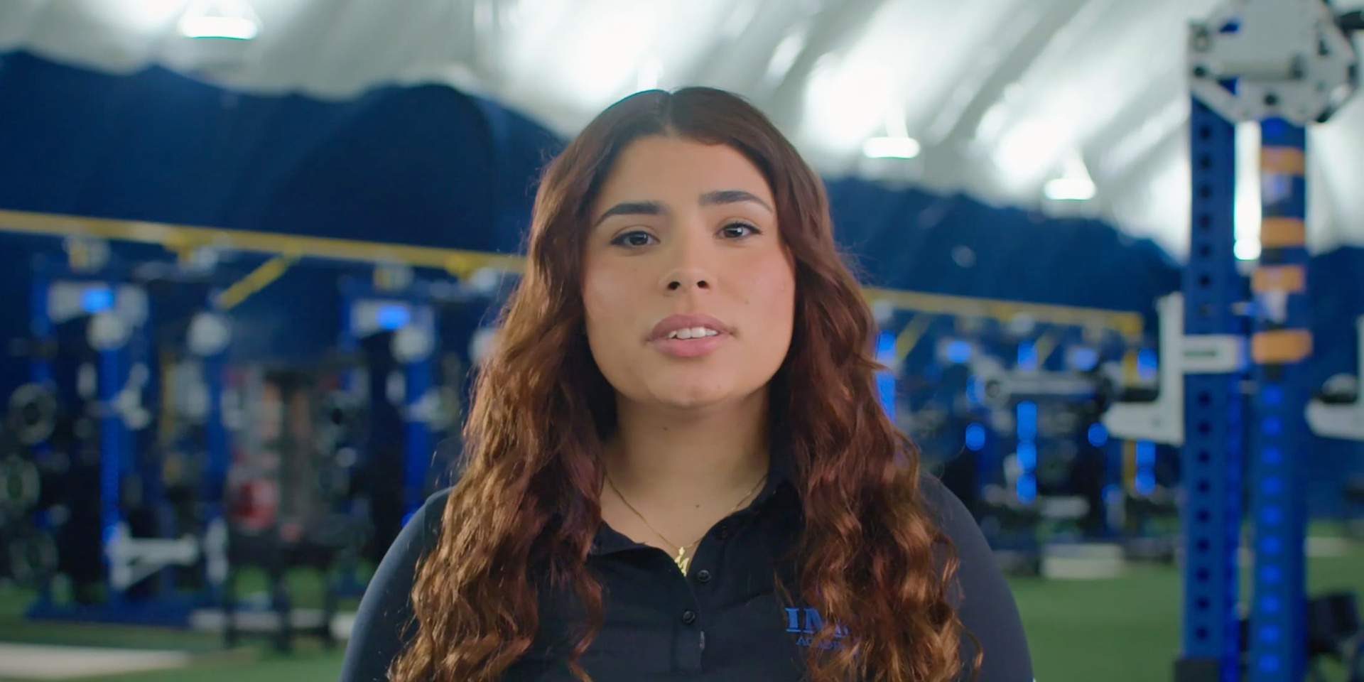 A trainer speaks to the camera in a weight room.