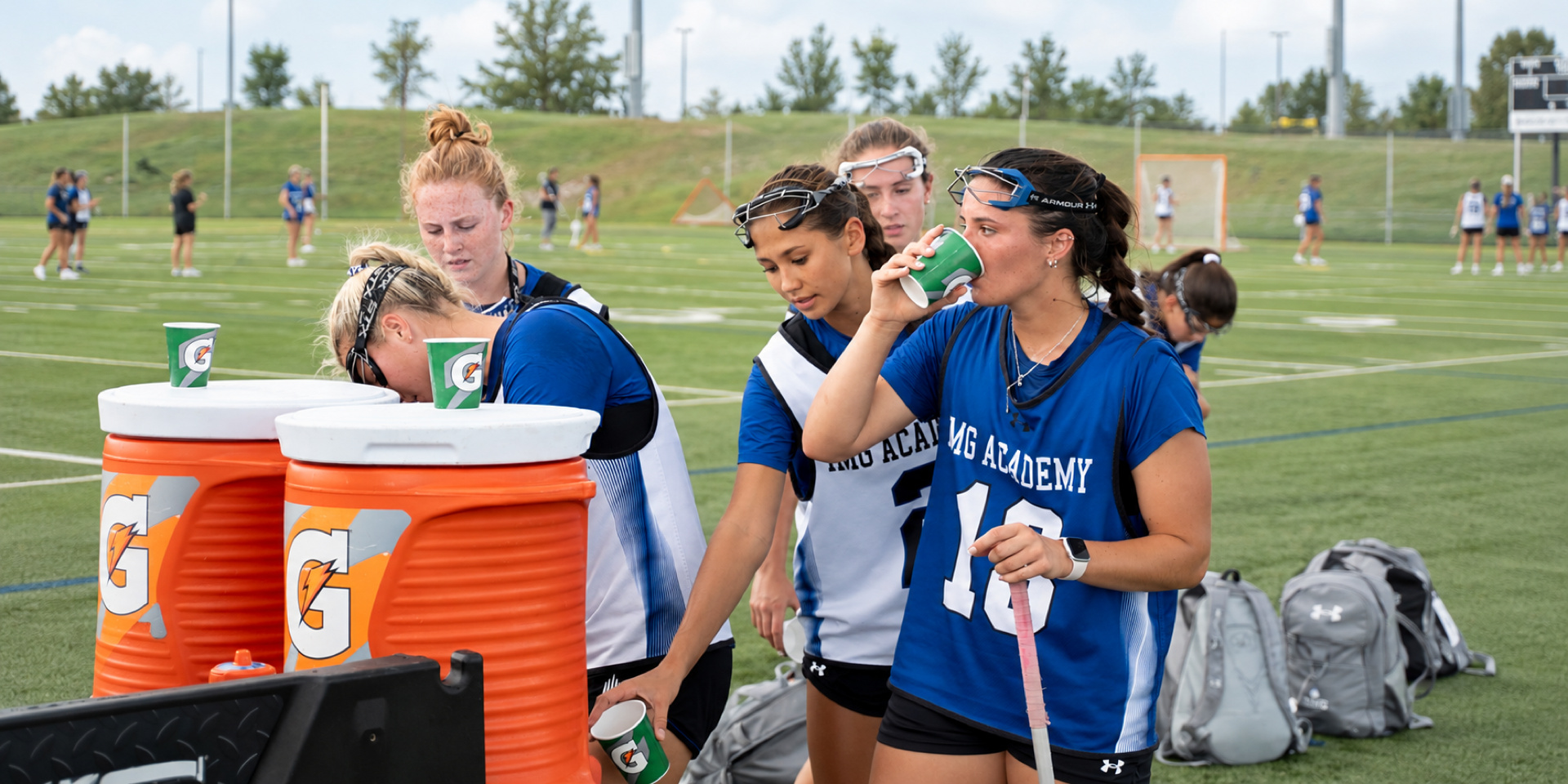 Athletes refill drinks from coolers during a break on the field.