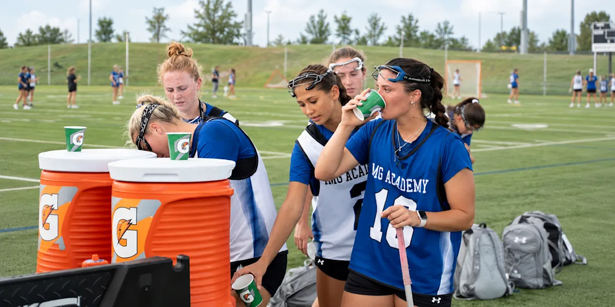 Athletes refill drinks from coolers during a break on the field.