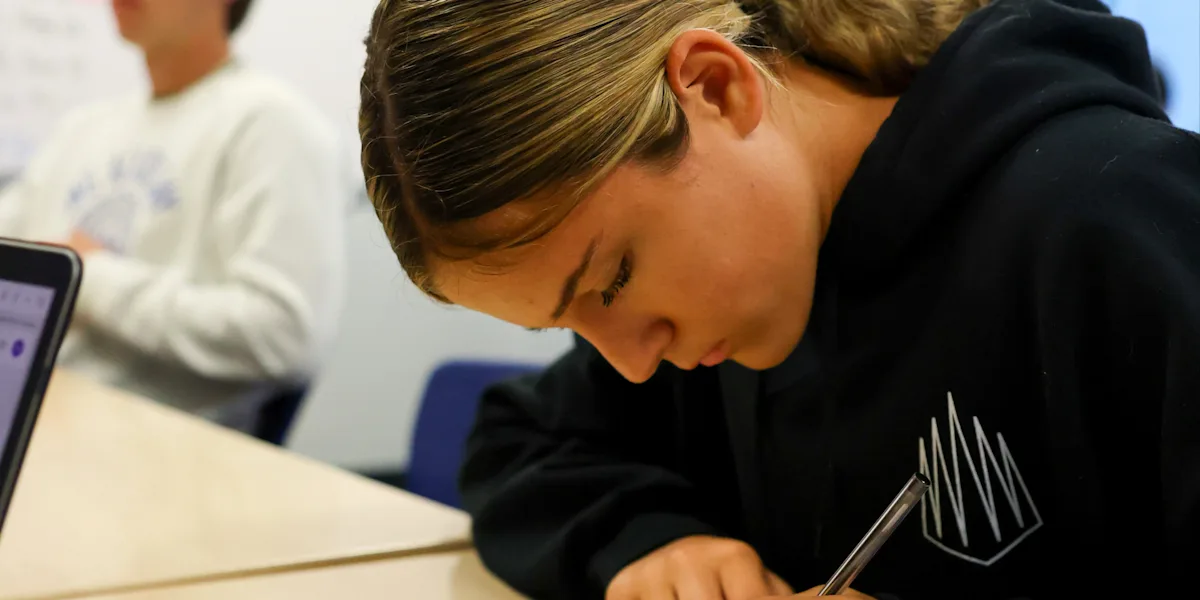 A student leans over a notebook while writing at a desk.