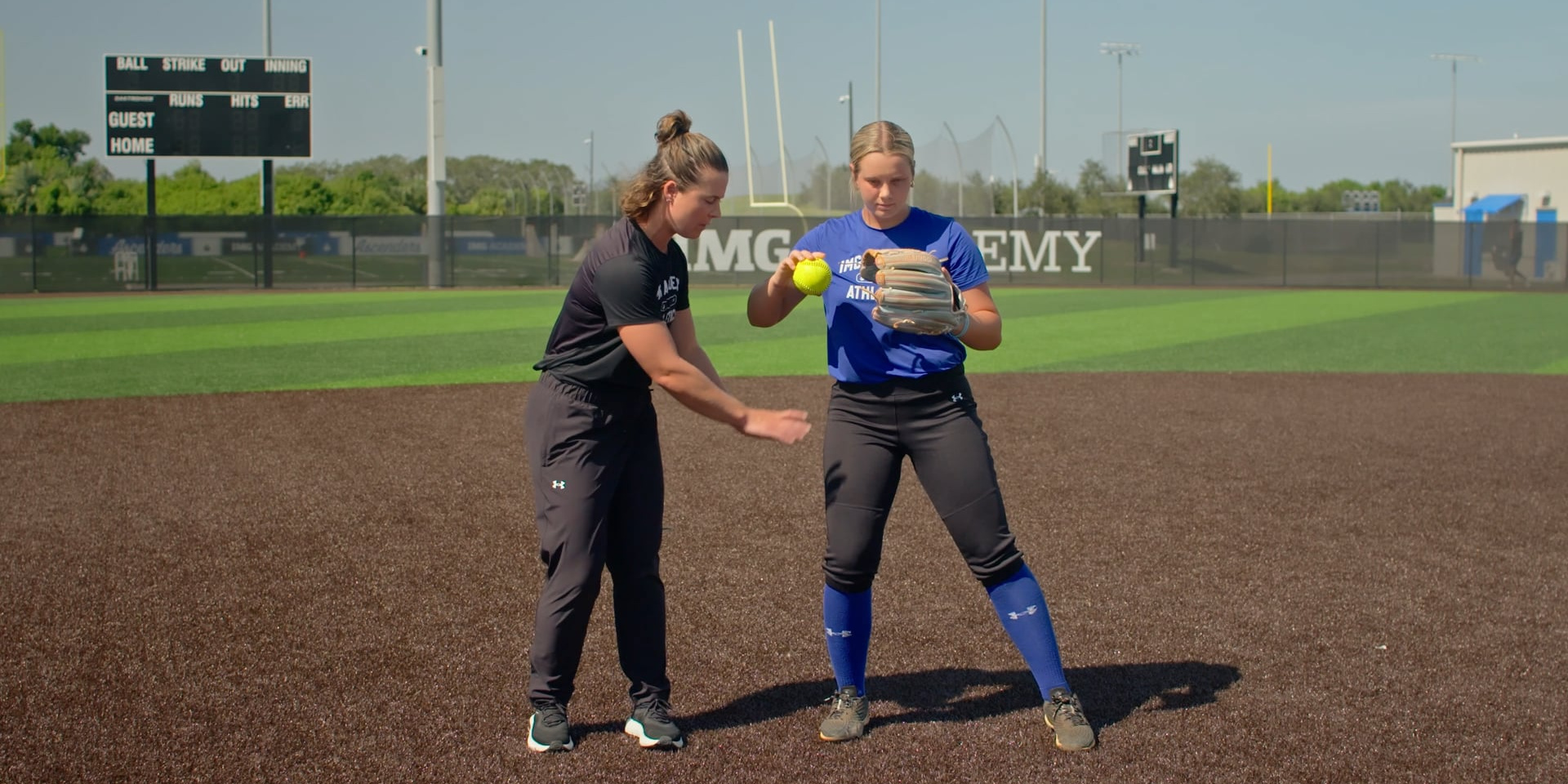 A softball coach guides a player through a throwing motion.
