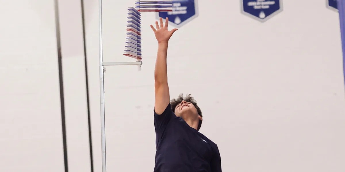 An athlete reaches upward toward a vertical-jump measuring device.