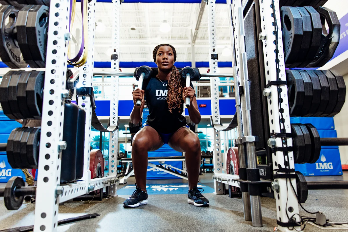 Female athlete performing a squat using a safety squat bar inside a weight room power rack.