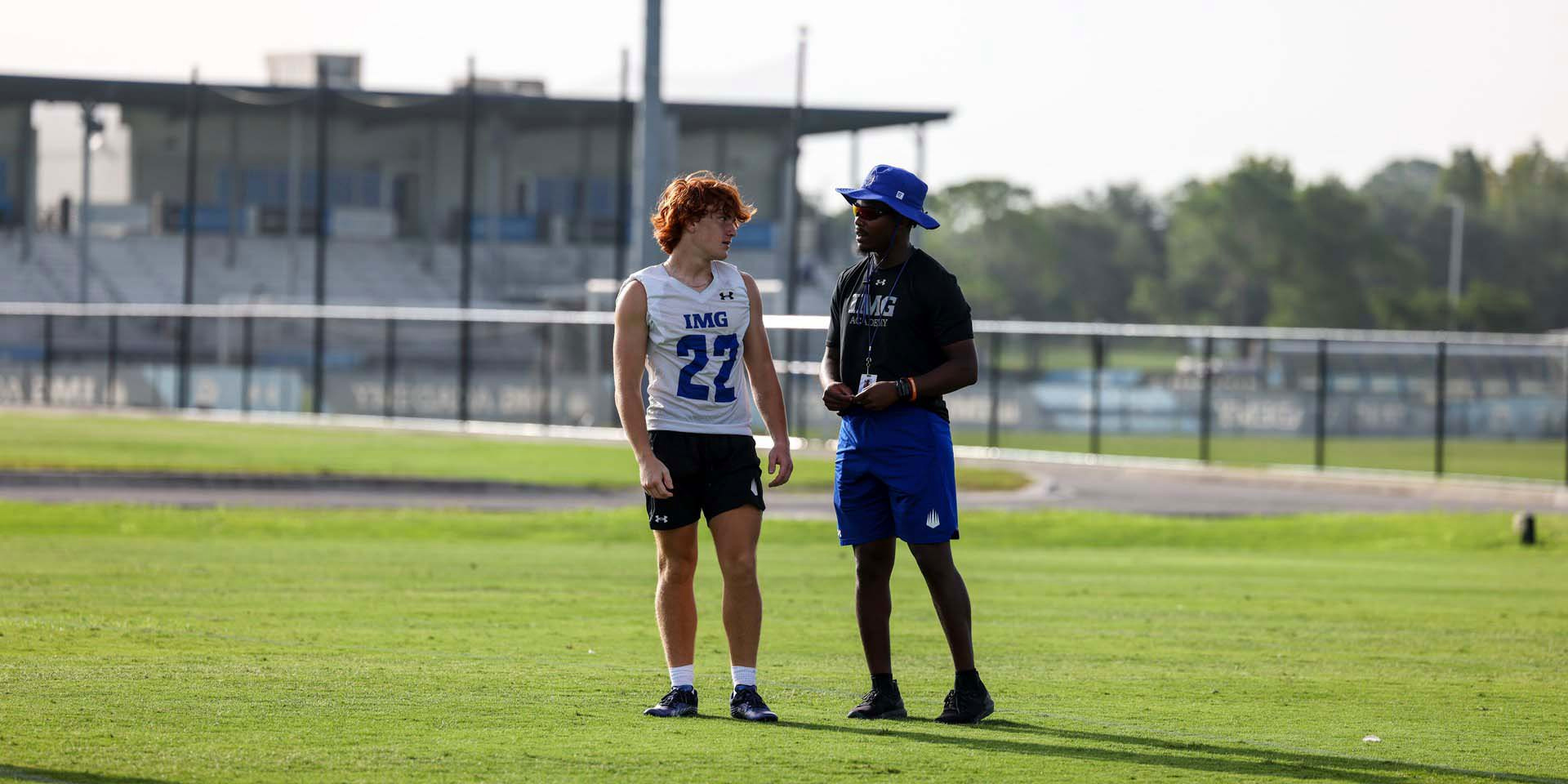 A coach and student-athlete talk together on the field.