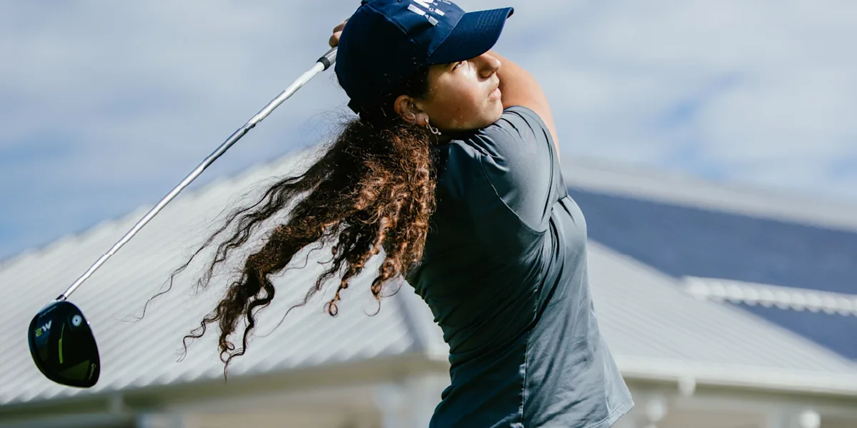 A golfer follows through on a drive beneath a cloudy sky.