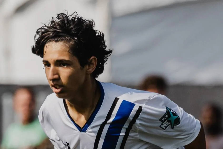 Focused male soccer player running during a match, wearing a white and blue uniform.