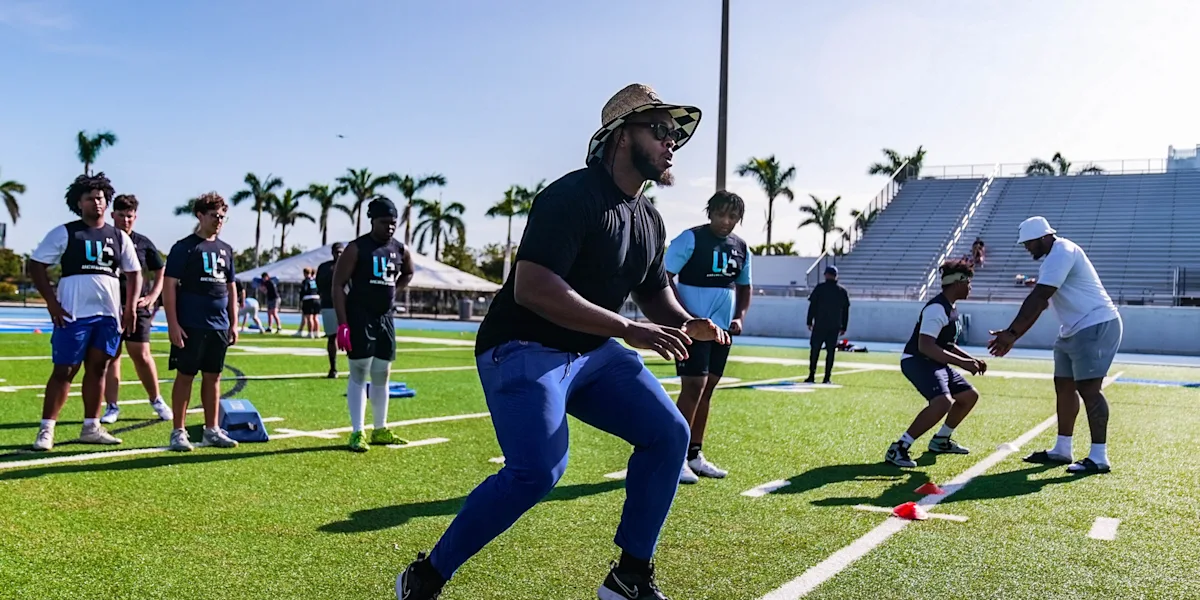 Athletes practice football footwork drills on a field.