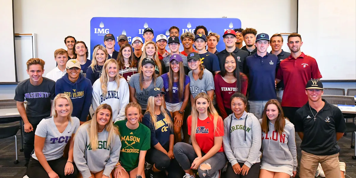A large group of student-athletes poses together wearing college shirts.