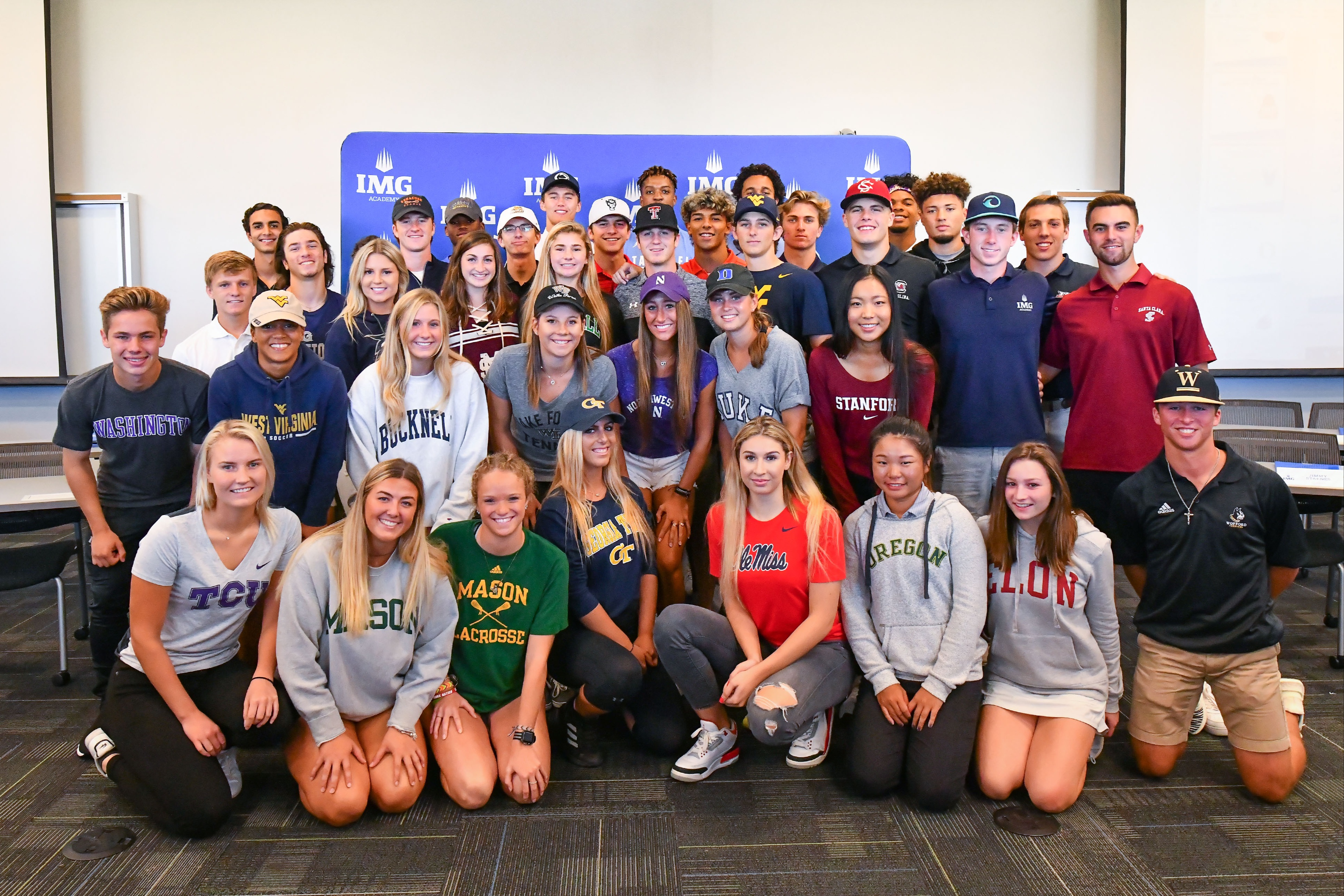 Group of IMG Academy student-athletes wearing college apparel, celebrating their recruitment to various NCAA programs across multiple sports.