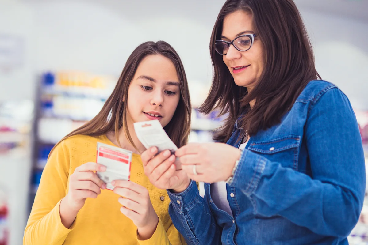 Mother and teenage daughter in a store aisle reading a product label or supplement information, emphasizing parental guidance in nutrition.
