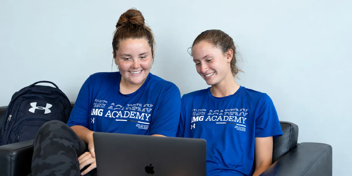 Two athletes smile while looking at a laptop together.