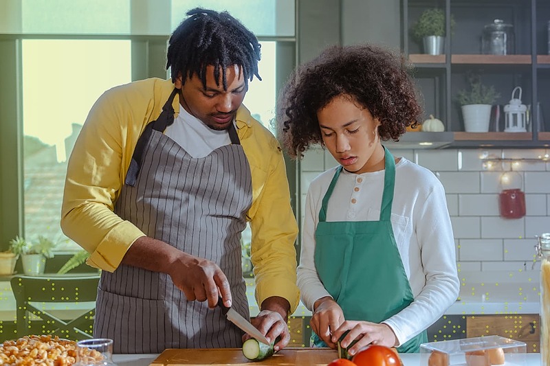 Parent and child preparing a healthy meal together in a kitchen, chopping fresh vegetables and learning cooking skills.