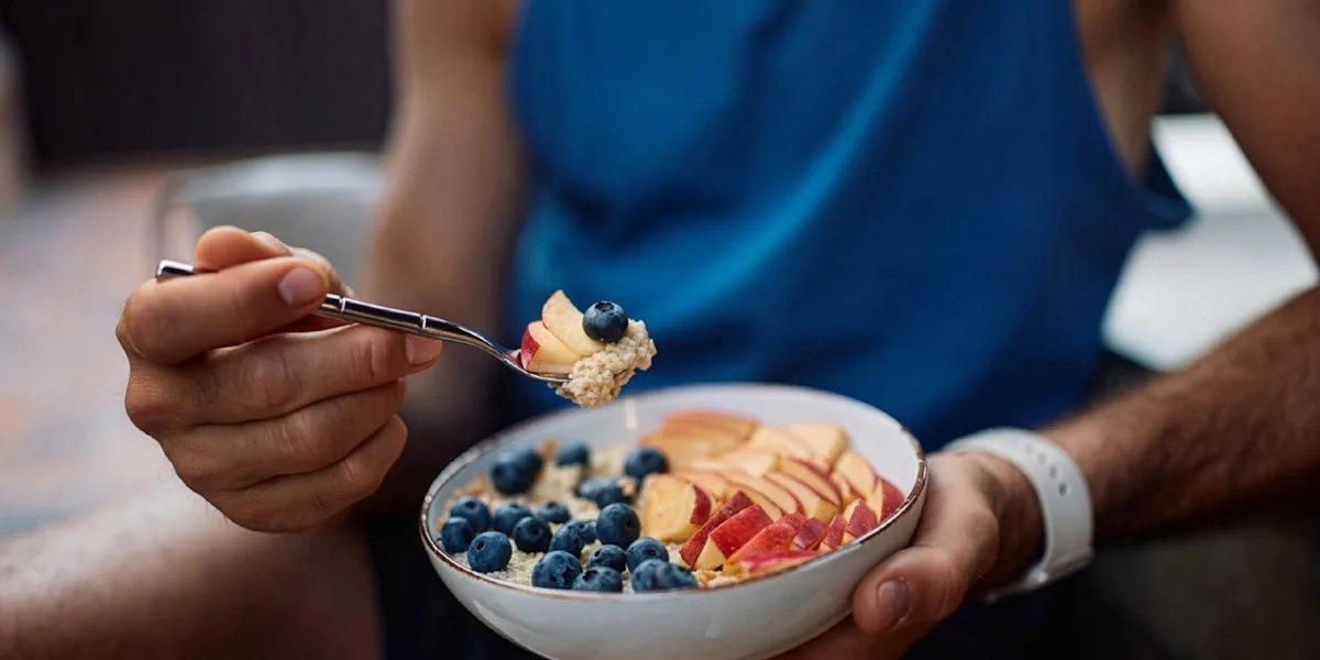 A close view shows an athlete eating a bowl of yogurt, fruit, and grains.