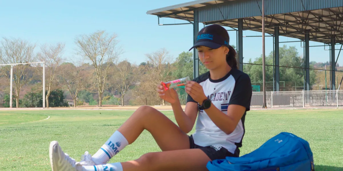 A seated athlete eats a slice of watermelon beside a sports bag.
