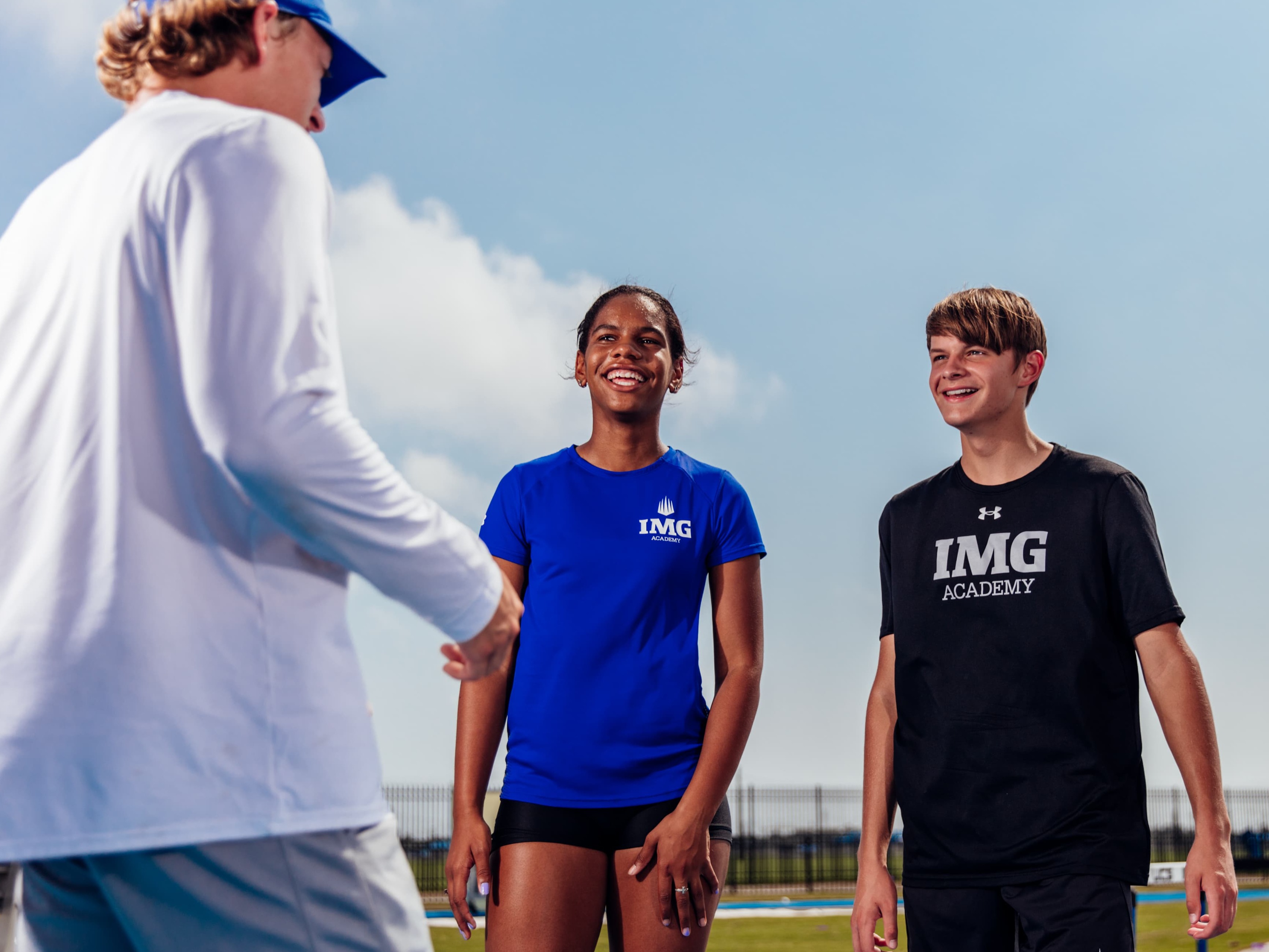 IMG Academy graphic featuring two smiling athletes talking to another athlete on a bright, sunny day