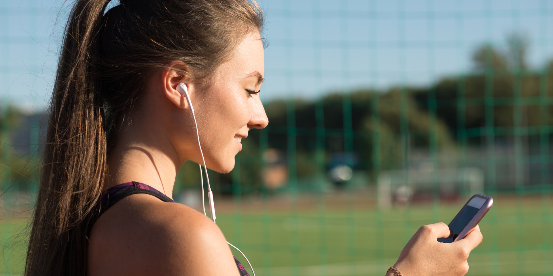 An athlete looks at her phone beside a sports field.