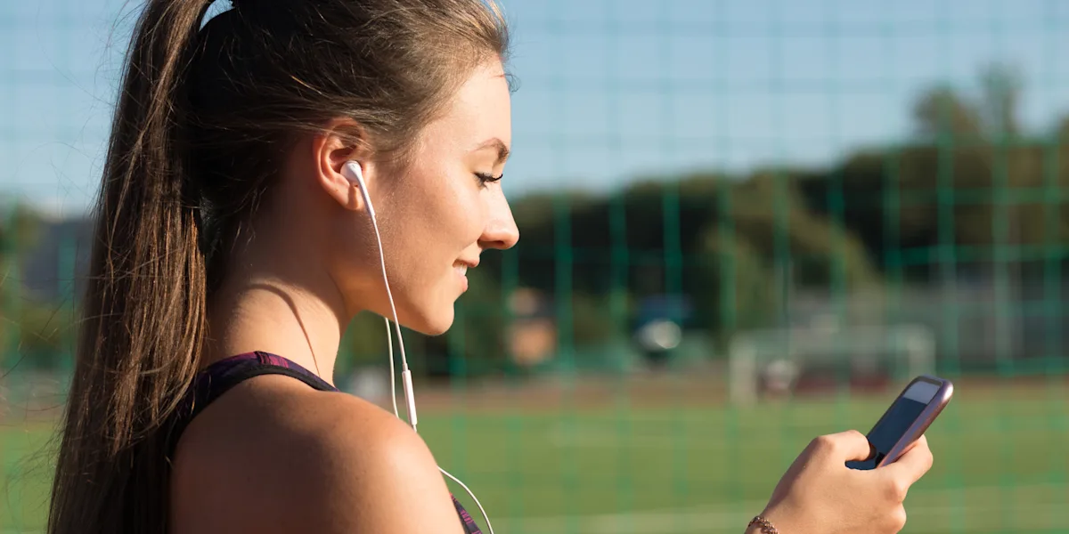 An athlete looks at her phone beside a sports field.
