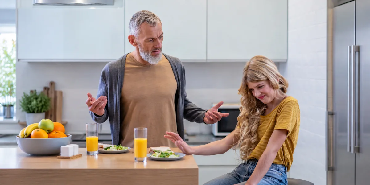 An adult talks with a young athlete at a kitchen counter set with breakfast foods.