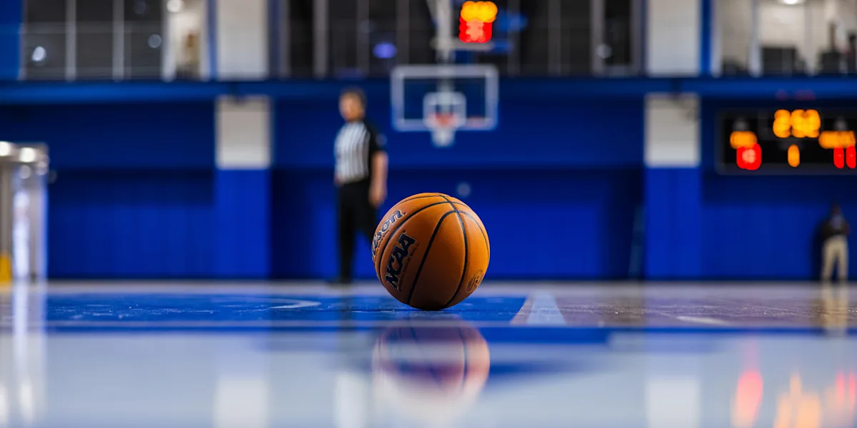 A basketball rests on the floor of an empty indoor court.
