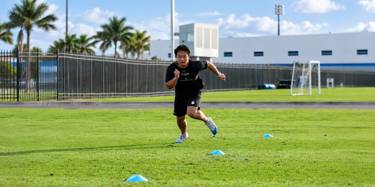 An athlete runs between cones on a grass field.