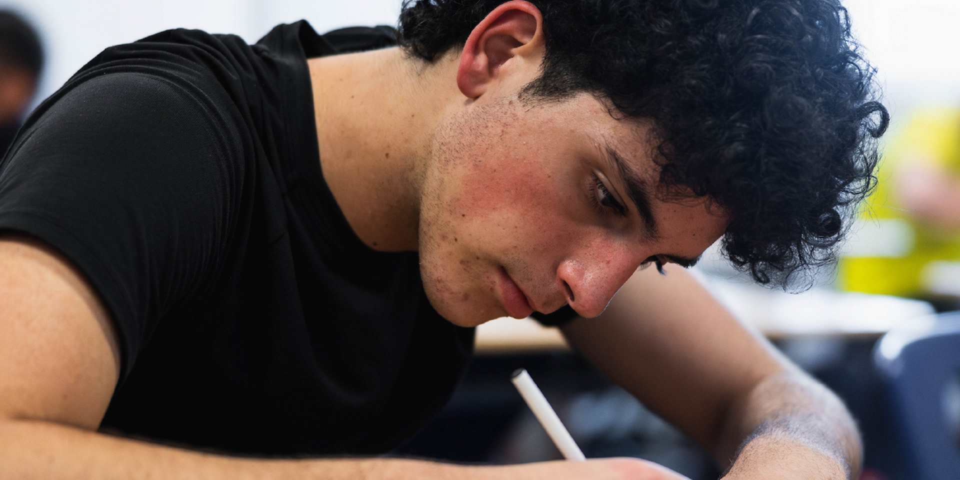 A student leans over his work while writing with a pencil.