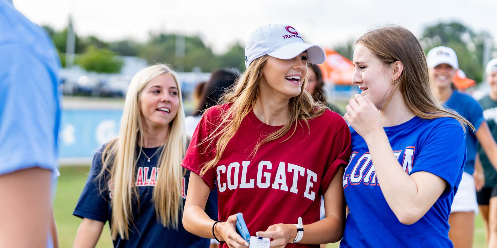 Three students smile and talk together at an outdoor event.