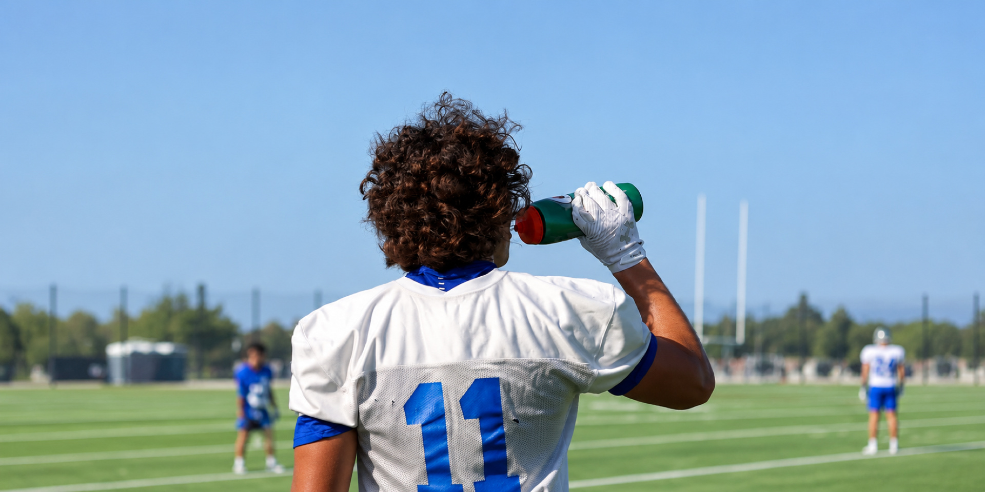 A football player drinks from a bottle during a break on an outdoor field.