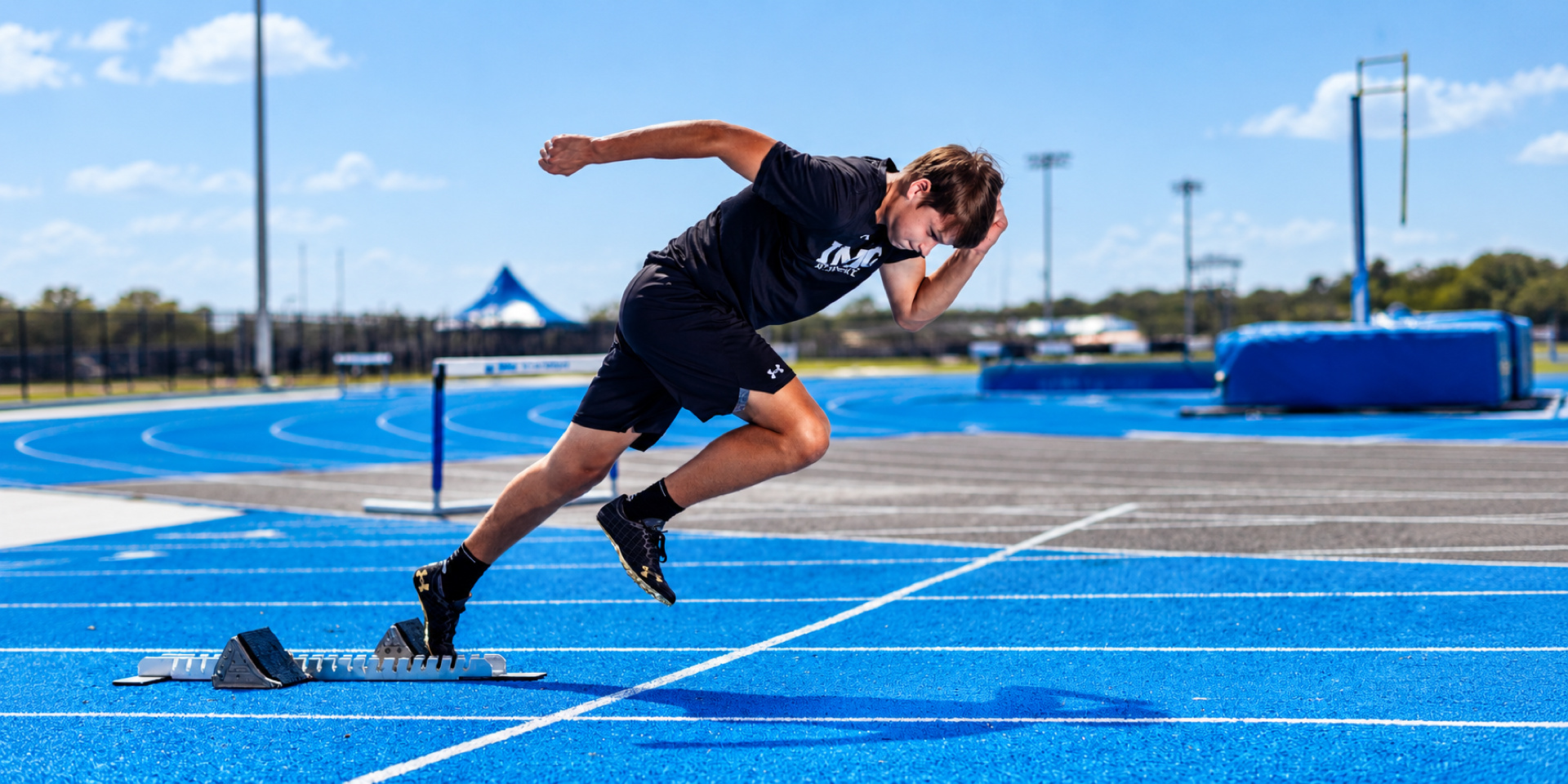 A sprinter accelerates out of starting blocks on a blue track.