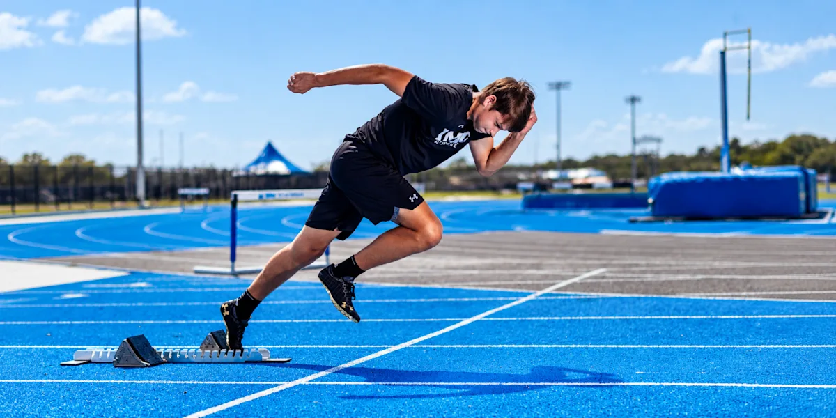 A sprinter accelerates out of starting blocks on a blue track.