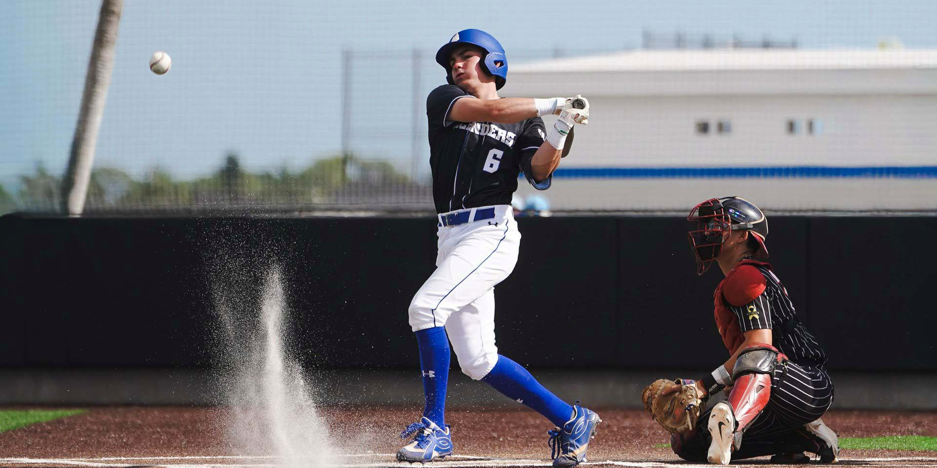 A baseball batter follows through on a swing as a catcher crouches behind him.