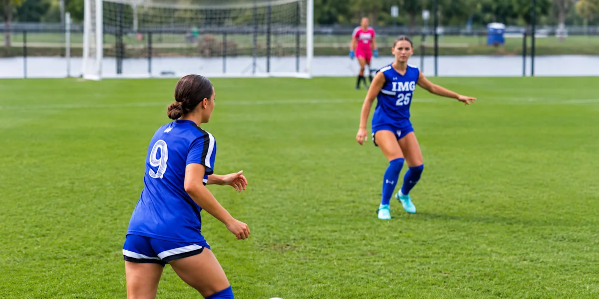 Soccer teammates pass a ball during practice on a grass field.