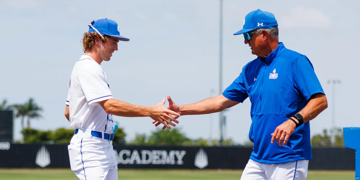 A baseball player shakes hands with a coach on the field.