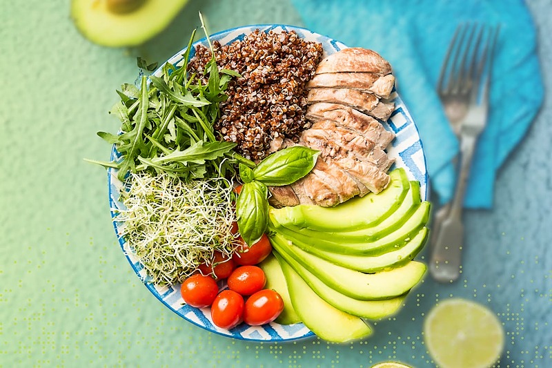 Balanced healthy meal bowl with grilled chicken, quinoa, avocado, leafy greens, sprouts, and cherry tomatoes, representing nutritious fueling for athletic performance.