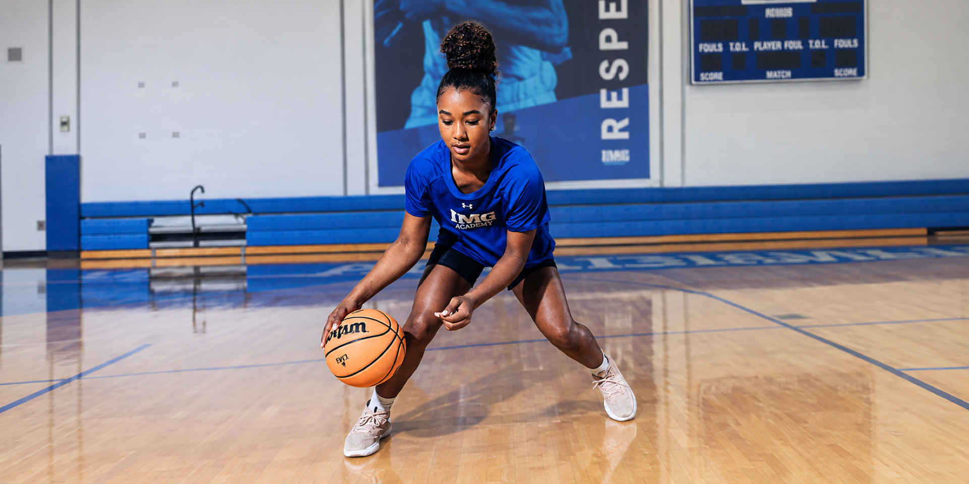 A basketball player crouches low while dribbling on an indoor court.