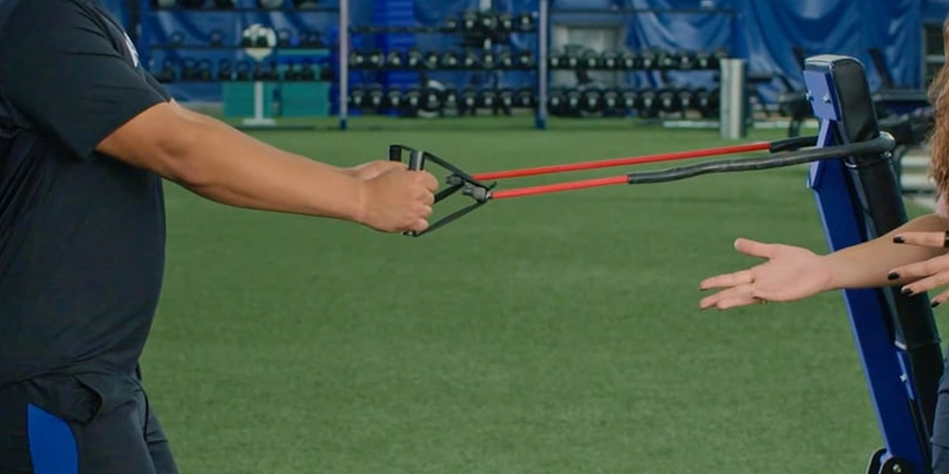 An athlete pulls resistance bands attached to a weight rack.