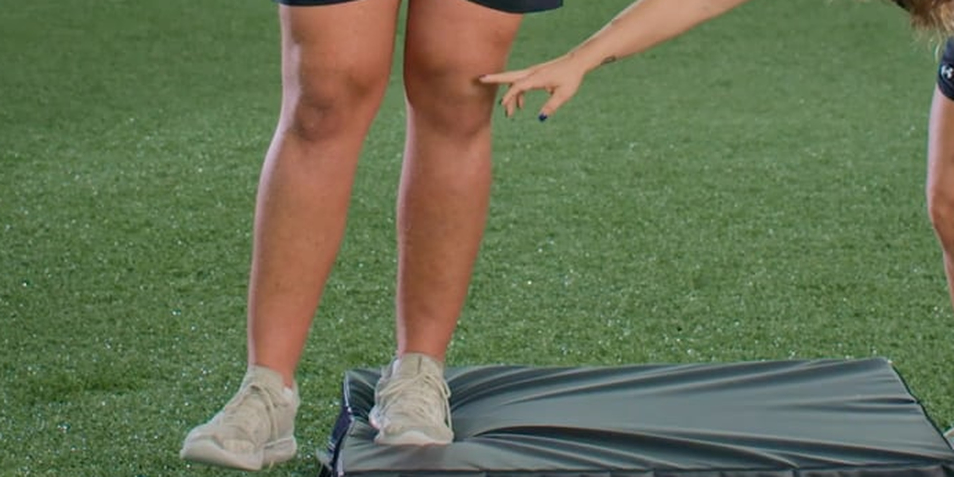 A trainer points to an athlete’s knee during a step-down exercise.
