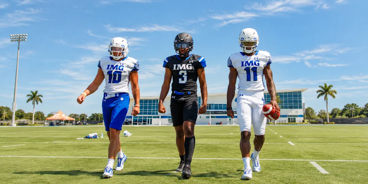 Three helmeted football players walk together across a field.