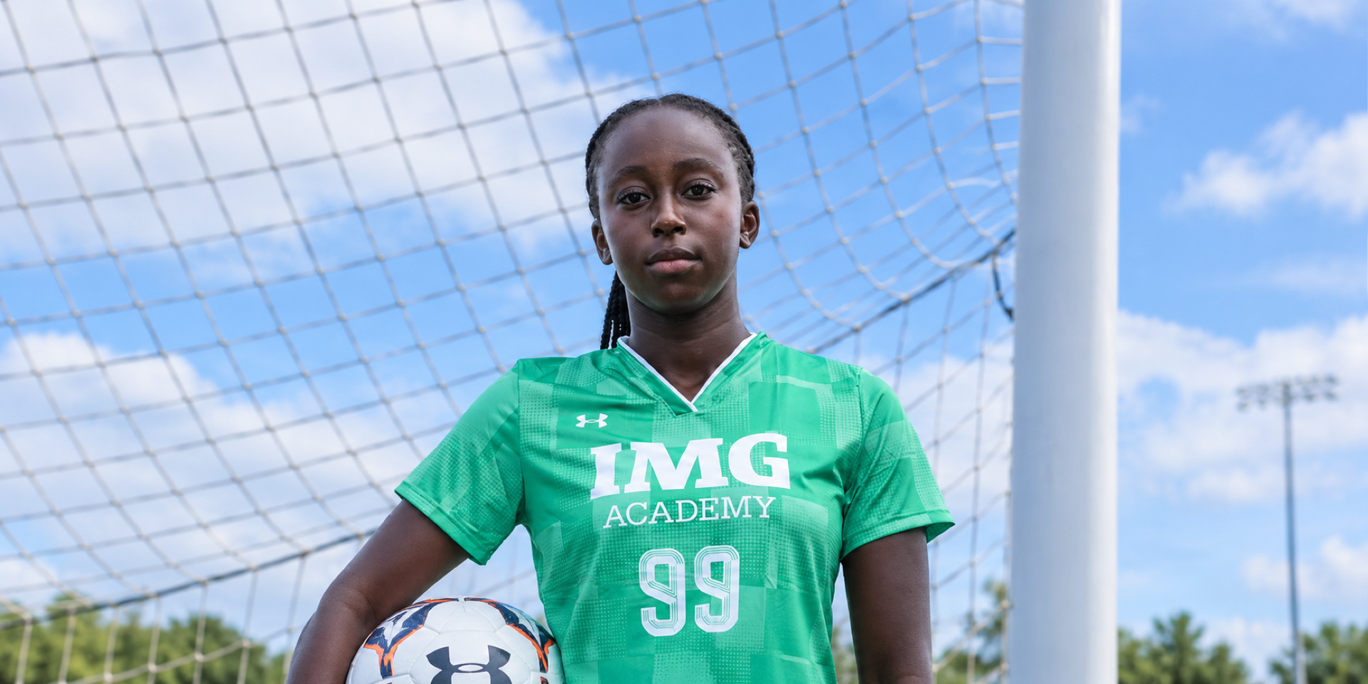 A soccer goalkeeper holds a ball while standing in front of a net.